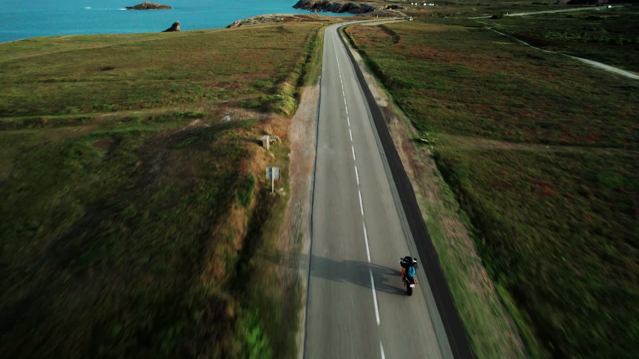 Une moto suivie au drone sur une route qui file vers la mer