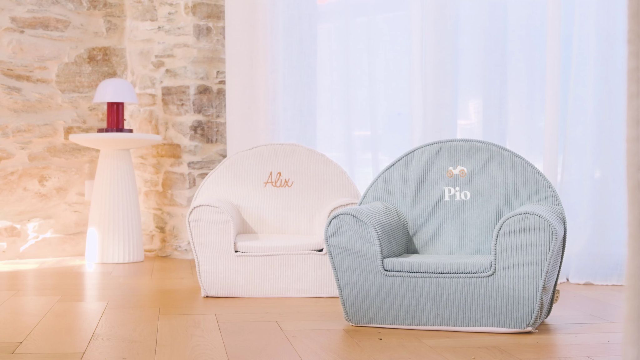 Deux fauteuils club Ma Petite Chaise, brodés Alix et Pio, devant un mur de pierre